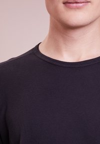 Black crew neck long-sleeve t-shirt made from textured fabric, featuring a ribbed neckline and fitted design.