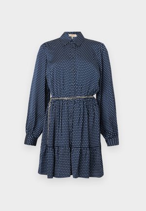 Robe à manches longues bleu marine à pois blancs, avec boutonnage sur le devant, jupe à volants et une fine ceinture chaîne à la taille.