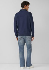 Maglione blu navy con collo e parte superiore della schiena a coste, abbinato a jeans denim svasati azzurri e sneakers bianche.