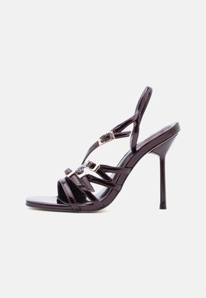 Fekete, magas sarkú, patentbőr szandál három elülső pánttal, arany csatbeszállítással és vékony bokapánttal, fehér háttéren.