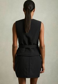 Svart ärmlös klänning med texturerad tyg, som har en figursydd midja och en lagerdesign på kjolen. Slät yta med synliga sömmar.