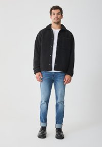 Juodas vilnos švarkas su apykakle ir krūtinės kišene, užsegamas mygtukais. Dėvimas ant baltos marškinės, derinamas su šviesiai mėlynomis džinsų kelnėmis ir juodais batais.