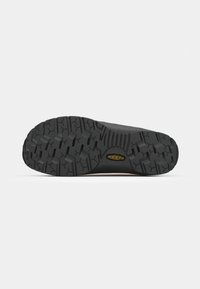 Black rubber outsole with multidirectional tread pattern, featuring a central logo. Sturdy design for traction and durability.