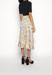 Haut court noir associé à une jupe midi fleurie avec un fond bleu clair et des fleurs multicolores ; mannequin portant des talons compensés noirs.