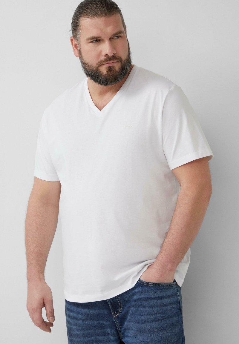 Witte katoenen V-hals T-shirt met korte mouwen, met een subtiel logo op de borst en een ontspannen pasvorm, gecombineerd met blauwe jeans.