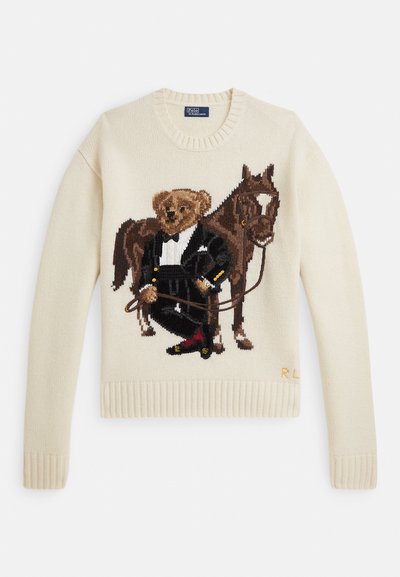 Kremowy sweter z dzianiny z misiem w smokingu, trzymającym wodze konia, stojącym obok brązowego konia z uzdą.