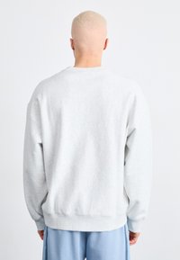 Sweatshirt gris clair avec une coupe décontractée, un col rond et des poignets et un ourlet côtelés. Fabriqué en tissu doux, présentant une texture lisse.