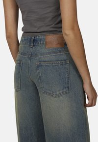 Lichtblauwe, high-waisted spijkerbroek met verchitte accenten, voorzien van een leren patch in bruin op de achterkant van de taille en standaard achterzakken.