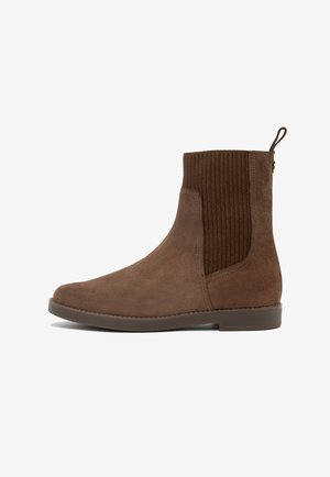 Braune Wildleder-Stiefelette mit gerippten elastischen Seitenpanels, abgerundeter Zehenpartie und einer Zuglasche an der Ferse. Flache Gummisohle, minimale Nähte.
