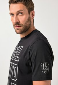 Černé bavlněné tričko s výrazným bílým nápisem a logem na levém rukávu, které se pyšní klasickým kulatým výstřihem a krátkými rukávy.