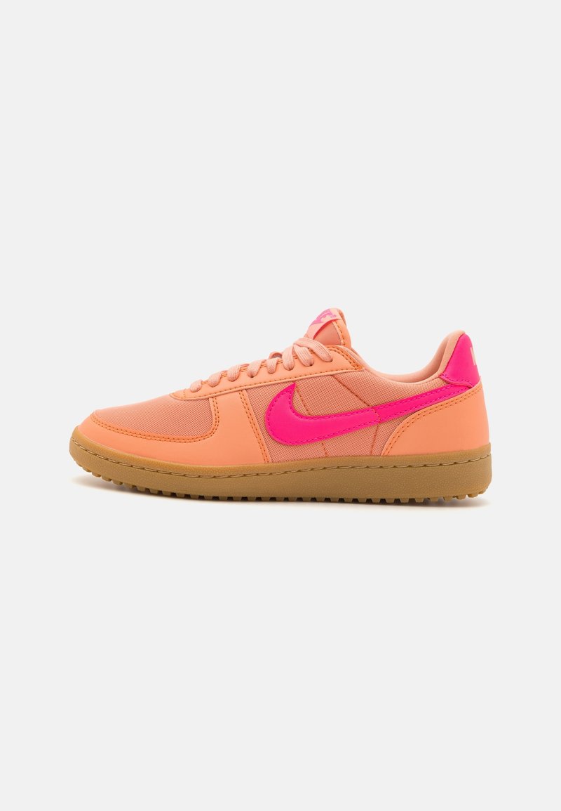 Baskets basses couleur pêche avec le swoosh Nike rose vif et une semelle en caoutchouc, affichées en profil latéral sur fond blanc.