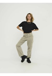 Zwarte cropped t-shirt gecombineerd met beige cargobroek met zijzakken. Draagt zwarte chunky veterboots. Neutrale achtergrond.