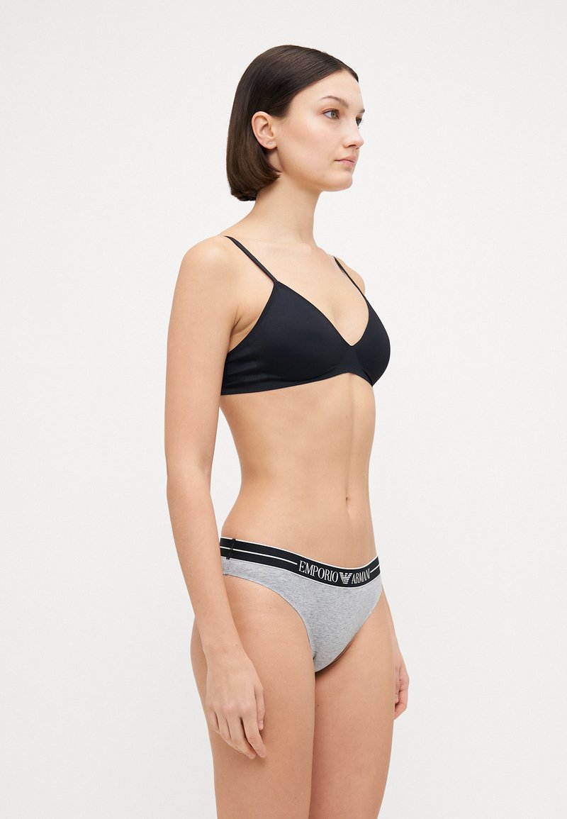 Bralette noir en forme de triangle avec des fines bretelles, associé à un slip gris avec une ceinture logo noire. Tissu lisse et design ajusté.