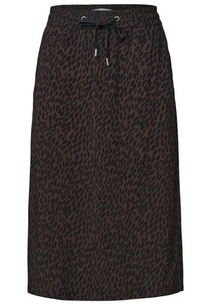 Taille et main d'une personne portant une chemise blanche et une jupe sombre avec des taches abstraites noires, présentant une ceinture élastique avec un cordon noir.