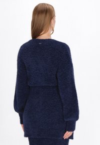 Granatowy, teksturowany sweter dzianinowy w skróconym fasonie, z długimi rękawami i dopasowaną talią; posiada subtelne logo na plecach.