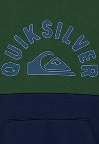 Zelená a námořnická mikina s kapucí, která má velké modré vyšívané logo "Quiksilver" a detail vlny. Jemná textura s kontrastními barevnými bloky.