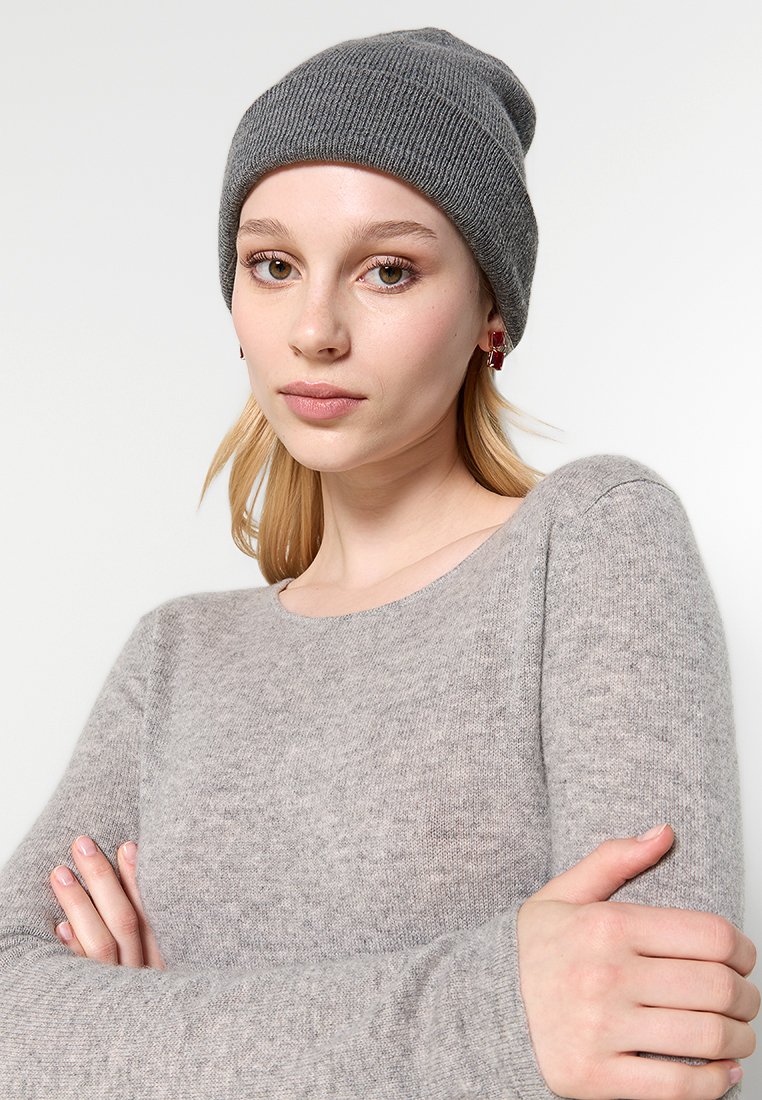 Szara dzianinowa czapka z prążkowanym wzorem, w zestawieniu z jasnoszarym swetrem z długim rękawem. Model pozuje z rękami skrzyżowanymi, prezentując oba elementy odzieży.