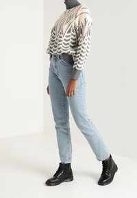 Mysig stickad tröja med ett zickzackmönster i beige och grått, kombinerad med ljusblå denimjeans och svarta snörda ankelskor.