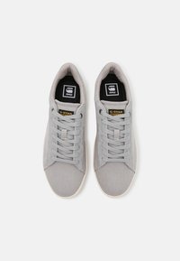Grey sneakers with a canvas upper, round toe, thick laces, and a textured surface. Features a black and white logo on the tongue.