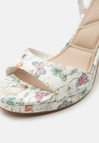 Sandalia cuña blanca de punta abierta con estampado multicolor de flores y mariposas y plantilla beige acolchada.