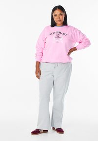 Svetlo roza pulover iz flisa z napisom »PERFORMANCE« spredaj, kombiniran s svetlo sivimi trenirkami in bordo supergami. Gladek tekstura.