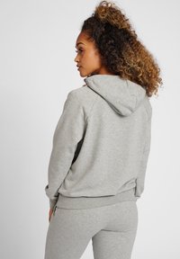 Grå sweatshirt med huva, som har en mjuk textur och avslappnad passform. Modellen visas från baksidan, vilket framhäver designen och färgen.
