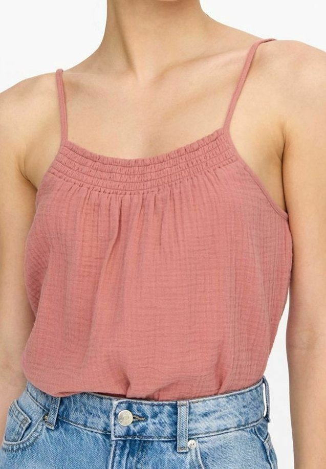 Haut sans manches rose poussiéreux avec un col froncé et un tissu léger texturé ; associé à un short en jean bleu clair taille haute.
