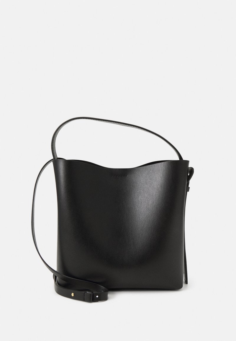 Sac seau en cuir noir avec un bord supérieur incurvé et une bandoulière réglable sur un fond clair uni.