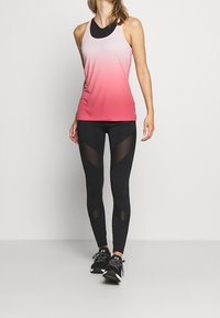 Red gradient athletic tank top with racerback design, paired with black leggings featuring mesh triangular inserts and black athletic shoes.