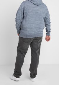 Gray hooded sweatshirt made of textured fabric, paired with loose-fit gray pants and white sneakers, viewed from the back.