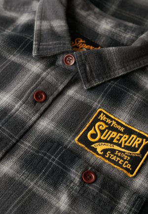 Grau und schwarz kariertes Flanellhemd mit braunen Knöpfen und einem gestickten gelben Superdry-Logo-Patch auf der Brust.