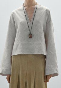 Chemise à manches longues rayée gris clair avec un décolleté en V et un ourlet court, associée à une jupe plissée beige taille haute. Collier pendentif inclus.