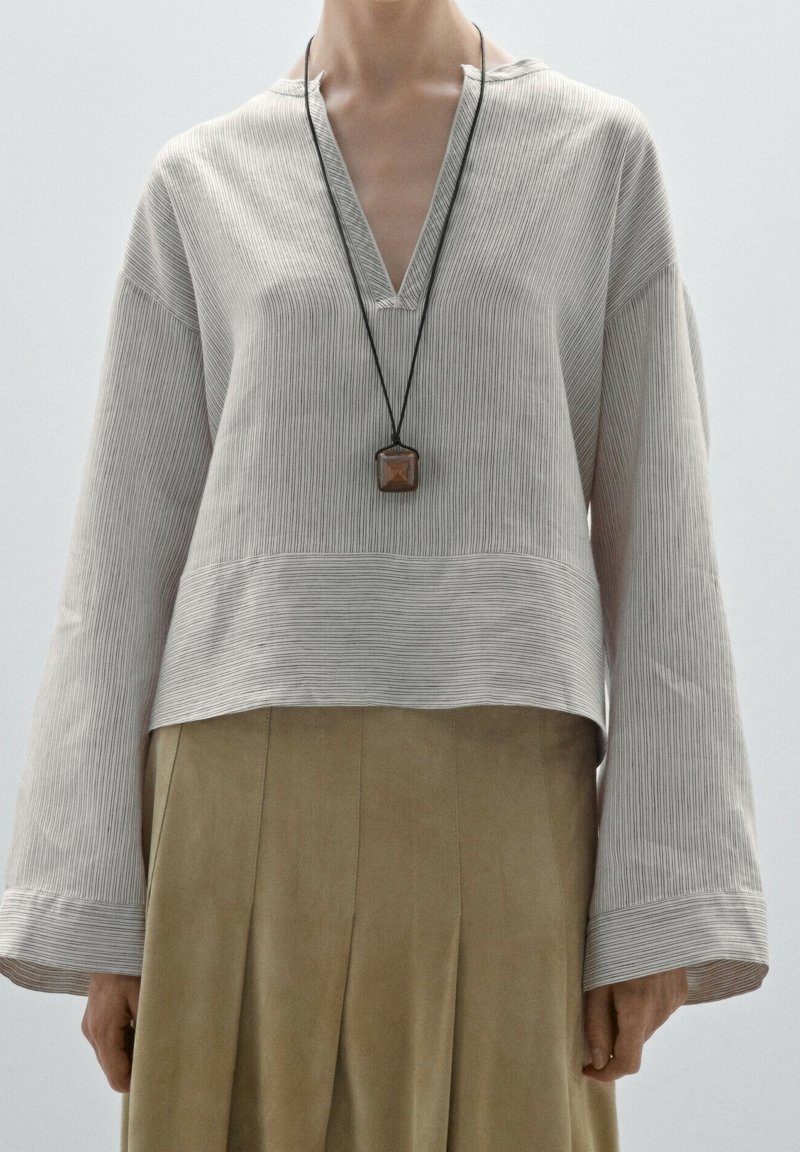 Chemise à manches longues rayée gris clair avec un décolleté en V et un ourlet court, associée à une jupe plissée beige taille haute. Collier pendentif inclus.