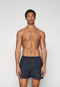Marineblaue Badehosen mit elastischem Bund, featuring Details mit vorderem Knopf, leichtem Stoff und einem schlichten Design.