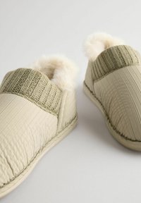 Beige quiltede slippers med ribbede strikkede detaljer og blød kunstpelsfor, der har en rund form og en fleksibel sål.