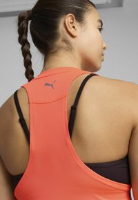 Puma tanktop i klart orange mesh-stof med sorte stropper. Har en lav rygdesign og et lille logo på den øverste ryg.