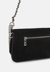 Mustan mokkanahkaisen käsilaukun hopeanvärinen ketjuolkaint. Vetoketjullinen etutasku ja sileä, mattapintainen tekstuuri. Moderni, kulmikas muoto.