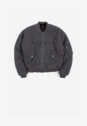 Tumši pelēka bombera jaka ar priekšējo rāvējslēdzēju, kabatām ar spiedpogām, rāvējslēdzēja kabatu uz piedurknes, ribota apdare aprocēs un apakšmalā, kā arī izšuvumu ar tekstu uz krūtīm.