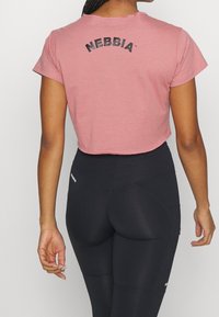 Camiseta recortada rosa con el logo "NEBBIA" en negro en la parte de atrás, combinada con leggings negros de cintura alta con acentos de logo.
