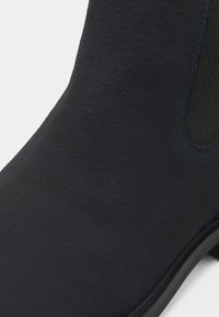 Gros plan d'une botte Chelsea en daim noir montrant un panneau latéral élastique et un bord de semelle texturé.