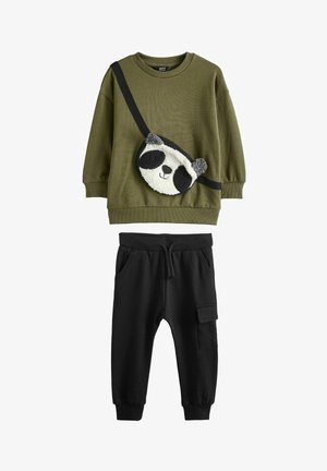 Olívazöld pulóver, pandaképű plüss zsebbel, és fekete, zsebes melegítőnadrág. A szett laza szabású és puha anyagú.