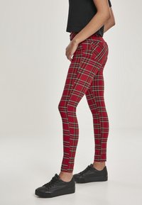 Leggings à carreaux rouges avec des rayures noires, présentant un design ajusté, des poches arrière cousues, portées avec des baskets noires. Texture lisse.