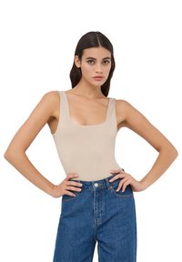Body beige con scollo quadrato e spalline larghe, abbinato a jeans blu a vita alta con chiusura frontale a bottoni e cuciture classiche.