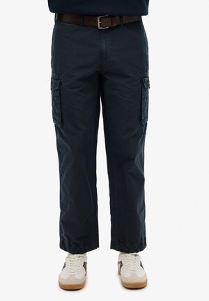 Pantalones de carga color navy con dos bolsillos laterales, puños ajustables en los tobillos y un cinturón marrón. Se llevan con zapatillas blancas y beige.