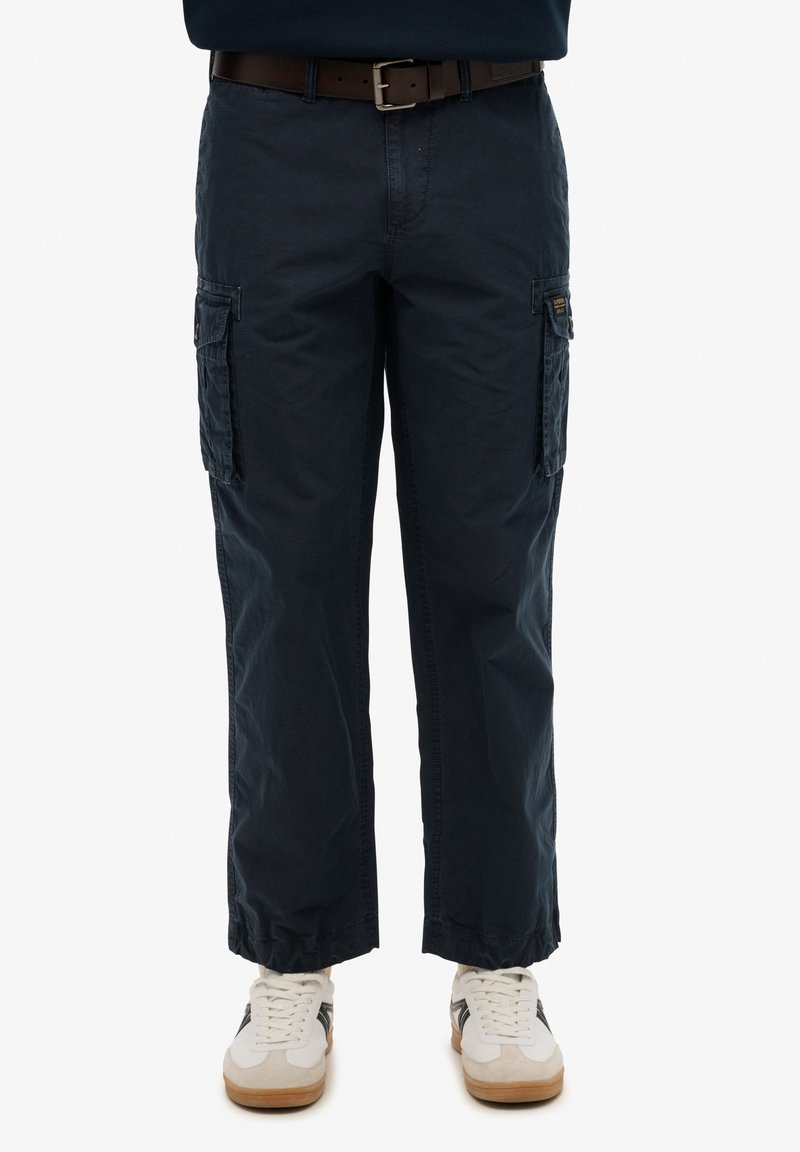 Marine cargo bukser med to sidelommer, justerbare ankle cuffs og et brunt bælte. Båret med hvide og beige sneakers.