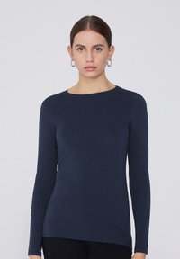 Camisa de manga larga azul marino con escote redondo, hecha de tejido suave y con un diseño entallado. Sin patrones visibles ni detalles metálicos.