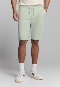 Licht mintgroene shorts met een elastische tailleband en trekkoord, met een gladde textuur en een knielange pasvorm. Gemaakt in combinatie met witte sokken en sneakers.