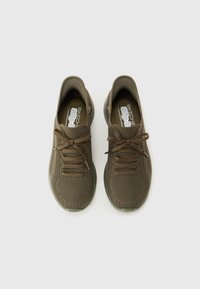 Poros pora alyvuogių spalvos Skechers slip-on megztų sportbačių su raišteliais, matomų iš viršaus, ant balto fono.