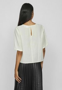 Top blanco de manga corta con detalle de abertura en la parte posterior, tejido texturizado y un dobladillo ligeramente recortado, combinado con una falda plisada negra.