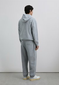 Pantalones deportivos y sudadera con capucha de color gris, confeccionados con tela suave, que presentan un ajuste holgado, bolsillos laterales y detalles de costuras visibles.